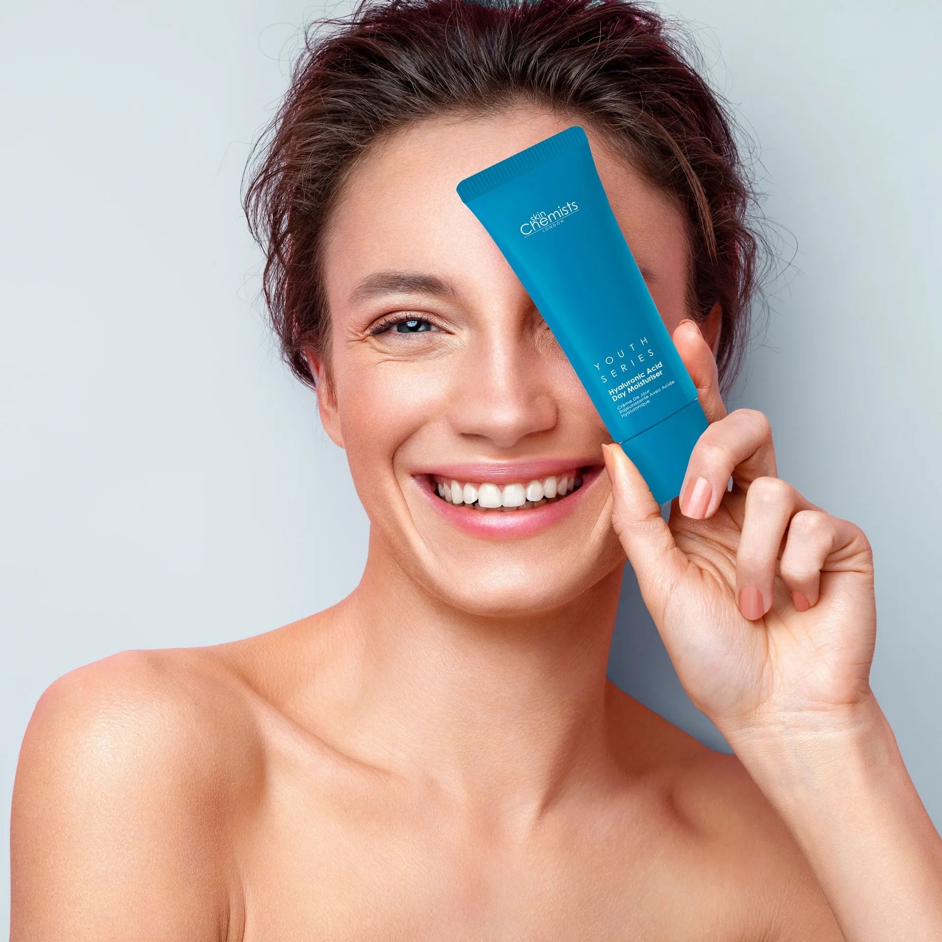 Woman holding a blue skincare product with a gray background